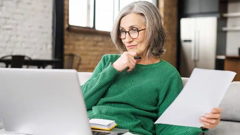 serious senior accountant sitting on the living room and looking at the laptop
